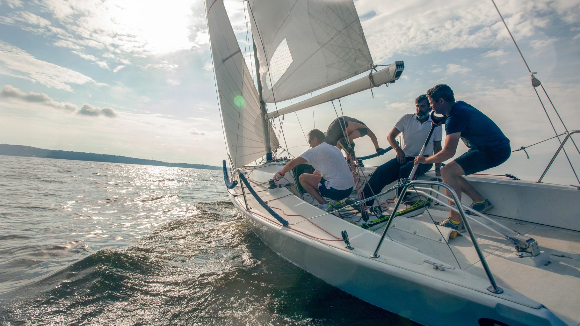 Vier Personen steuern ein Segelschiff im Wind