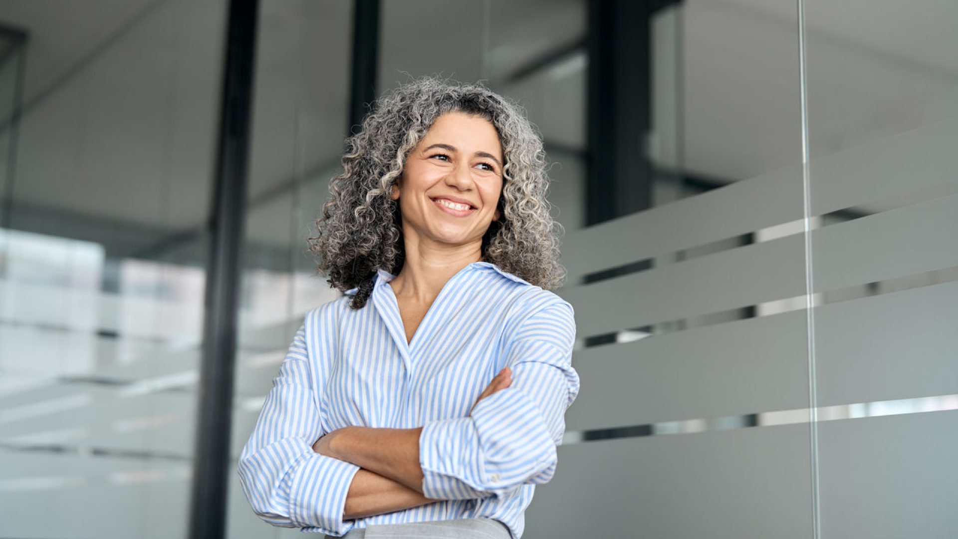 Happy mature professional business woman leader standing in office looking away.